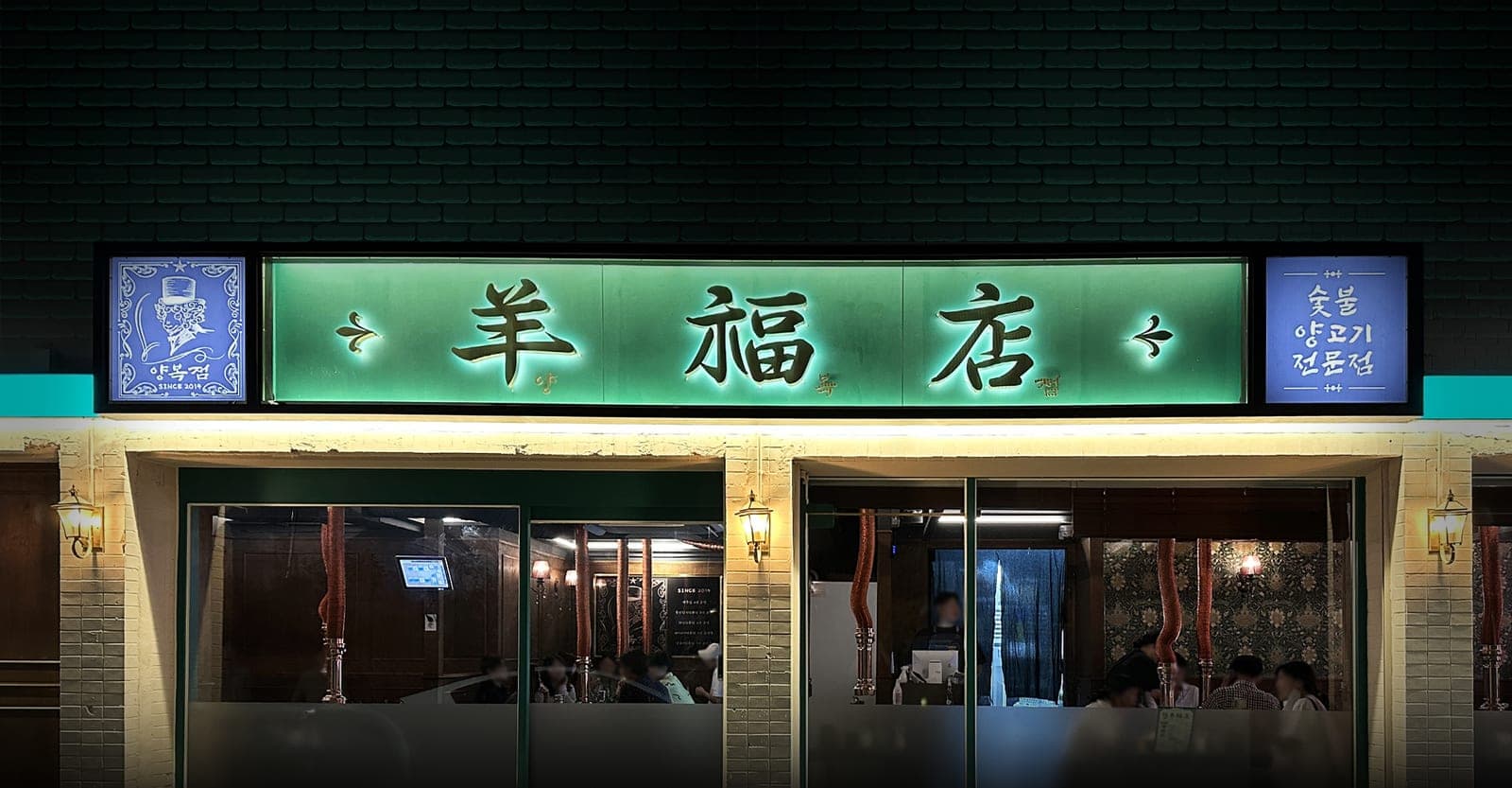 밤에 불이 켜진 羊福店 간판과 통유리 너머로 보이는 매장 안 손님들